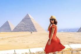 Woman in a red dress and sun hat walking in front of the Giza pyramids
