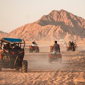 Quad bikes and a buggy kicking up sand in the desert near Dahab at sunset