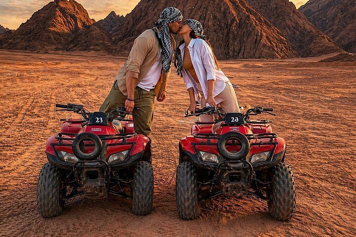 Couple in desert scarves leaning together between two red quad bikes at sunset