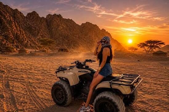 Woman sitting on a quad bike in the desert at sunset, with mountains and acacia trees behind