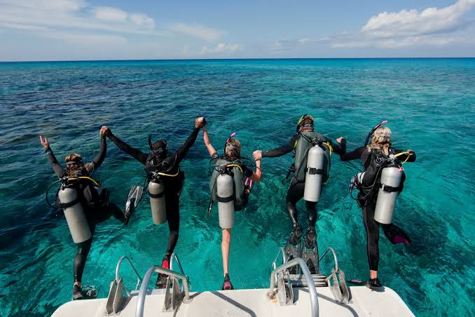 Groupe de plongeurs se tenant la main en sautant de l'arrière d'un bateau dans une eau turquoise