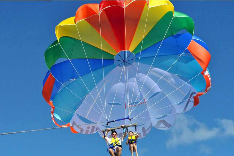 Deux personnes en gilet de sauvetage sous un parachute ascensionnel arc-en-ciel dans le ciel bleu