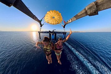 Deux personnes en parachute ascensionnel au-dessus de la mer au coucher du soleil, vues sous la voile jaune